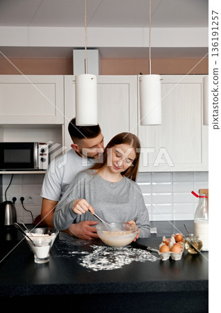 Couple enjoys a cozy baking session in their modern kitchen while preparing a delicious homemade treat together Couple enjoys a cozy baking session in their modern kitchen while preparing a delicious homemade treat together 136191257