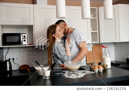 Couple enjoys a romantic moment while baking together in a modern kitchen during a cozy morning Couple enjoys a romantic moment while baking together in a modern kitchen during a cozy morning 136191258
