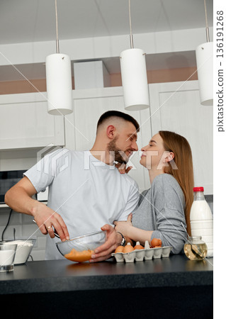 Young couple enjoys cooking together in a modern kitchen while sharing a laugh and preparing a meal with love and joy during a weekend at home 136191268