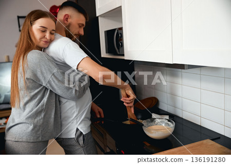 Couple cooks together in a modern kitchen during afternoon while preparing a meal and sharing a moment of warmth Couple cooks together in a modern kitchen during afternoon while preparing a meal and sharing a moment of warmth 136191280