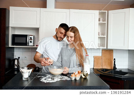 Couple preparing dough in a kitchen during daylight while engaging in cooking conversation and enjoying the process together 136191284