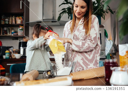 Mother and daughter bake together in a kitchen filled with supplies as they share a moment of learning and fun during a weekend afternoon activity 136191351
