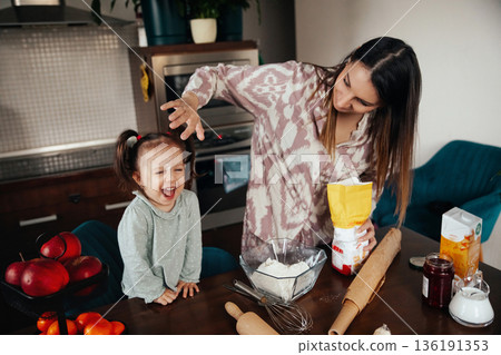 Young girl enjoys baking with mother in kitchen, laughing as they prepare ingredients for cookies on a weekend morning Young girl enjoys baking with mother in kitchen, laughing as they prepare ingredients for cookies on a weekend morning 136191353