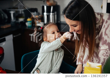 Child plays with flour and smiles at mother during cooking activity in a kitchen at home in the morning 136191357