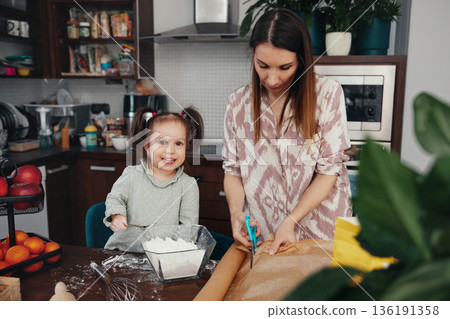 Mother and daughter prepare dough for baking in a kitchen filled with fruit and kitchen tools during daytime cooking session 136191358