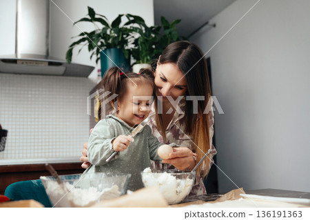 Mother and daughter baking together in a kitchen, enjoying time while preparing a fun recipe with various ingredients and smiles 136191363