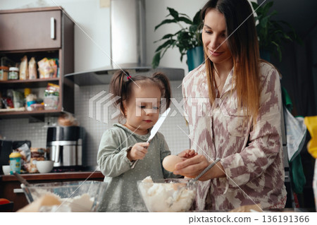 Mother and daughter cook together in kitchen preparing dough with eggs and flour in the morning sunlight Mother and daughter cook together in kitchen preparing dough with eggs and flour in the morning sunlight 136191366