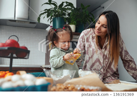 Mother and daughter prepare food together in a kitchen during the day while enjoying time spent on cooking and learning new things 136191369