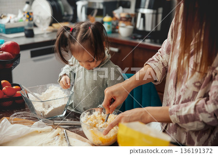 Mother and daughter prepare food together in a kitchen during daytime for a cooking activity with ingredients and tools present on the counter 136191372