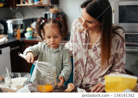 Mother and daughter baking together in kitchen while mixing ingredients and having fun in the afternoon Mother and daughter baking together in kitchen while mixing ingredients and having fun in the afternoon 136191382