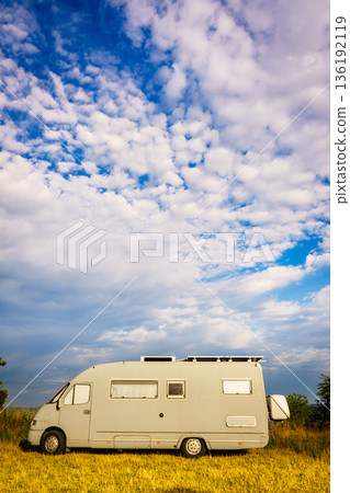 Camping car parked in a field with trees and blue sky during daytime in a rural area 136192119