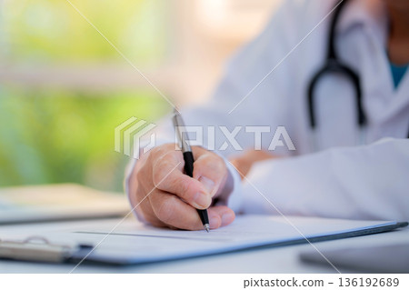 Close up senior asian doctor writing prescription or document on clipboard in clinic office. Close up senior asian doctor writing prescription or document on clipboard in clinic office. 136192689
