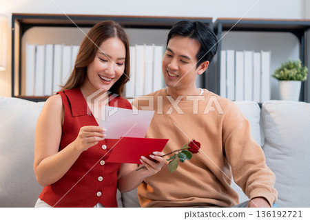 Happy asian couple sitting on sofa celebrating Valentine's Day with romantic surprise together. 136192721
