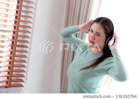 Happy young asian woman wearing headphones listening music while standing dancing with fun. 136192764