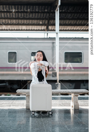 Woman sitting on bench with suitcase at train station, ready for travel and exploration. Woman sitting on bench with suitcase at train station, ready for travel and exploration. 136192779
