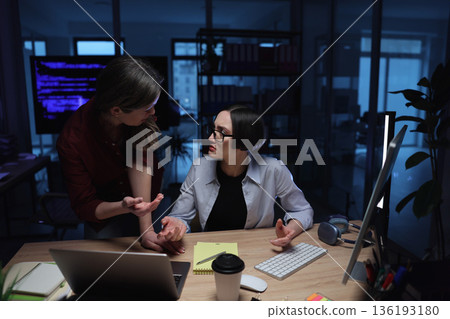 Women discussing ideas in a modern workspace late at night with glowing screens and a creative atmosphere 136193180
