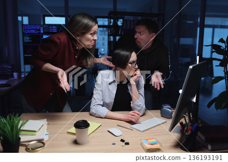 Three colleagues engage in a lively discussion while working late in a modern office during evening hours 136193191