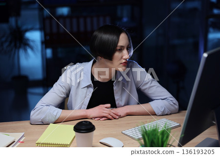 Late-night focus on the screen: a determined individual navigating a world of ideas and creativity from a cozy workspace Late-night focus on the screen: a determined individual navigating a world of ideas and creativity from a cozy workspace 136193205