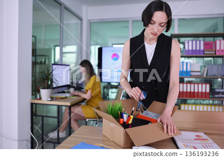 Office transformation moment as one woman unpacks a box while another works at the computer in a colorful workspace 136193236