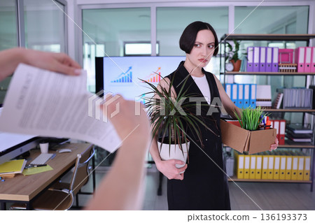 Woman with plants and boxes shows mixed emotions after office transition in a bright workspace filled with documents and charts Woman with plants and boxes shows mixed emotions after office transition in a bright workspace filled with documents and charts 136193373
