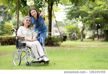 Young caucasian nurse comforting with patient while sitting on wheelchair in outdoor park. Young caucasian nurse comforting with patient while sitting on wheelchair in outdoor park. 136193394
