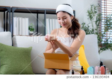 Young asian woman sitting on sofa test cosmetic cream or lotion with shopping online. Young asian woman sitting on sofa test cosmetic cream or lotion with shopping online. 136193404