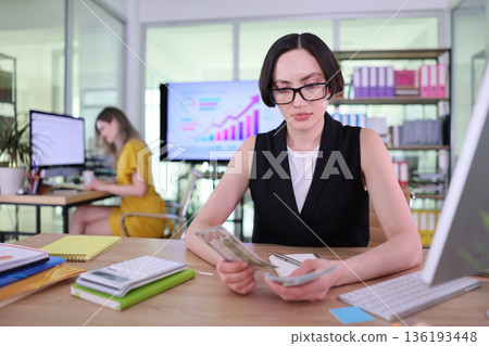 Focused woman analyzes financial data in a modern office space during a busy workday 136193448