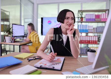 Woman expresses concern while analyzing data in a bright office during a busy workday Woman expresses concern while analyzing data in a bright office during a busy workday 136193458