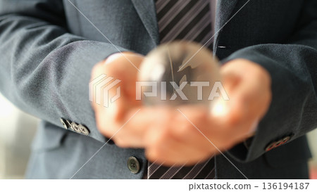 Business professional holds a crystal globe with a confident expression in a bright office during a morning meeting 136194187