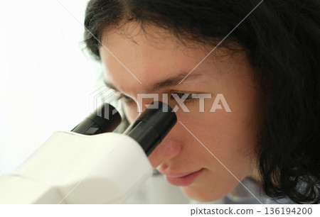 Young scientist explores the microscopic world with curiosity and focus in a bright laboratory setting 136194200