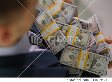 Person holds a large stack of cash in their arms, showcasing wealth and abundance in a sleek environment Person holds a large stack of cash in their arms, showcasing wealth and abundance in a sleek environment 136194210