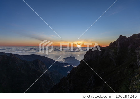 Sunrise scene from Pico do Arieiro as rugged peaks rise above clouds and calm ocean below horizon 136194249