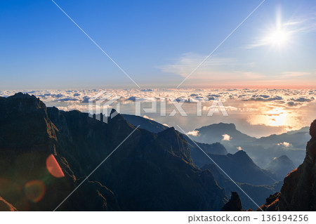 Colorful sunrise over Pico do Arieiro iconic ridge with sun rays lens flare and Atlantic clouds Colorful sunrise over Pico do Arieiro iconic ridge with sun rays lens flare and Atlantic clouds 136194256