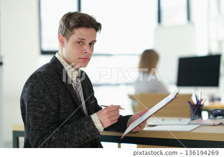 Focused young professional takes notes during a meeting in a bright, modern office setting filled with natural light Focused young professional takes notes during a meeting in a bright, modern office setting filled with natural light 136194269