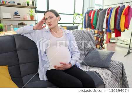 Pregnant woman relaxing on a couch surrounded by colorful clothing in a bright, airy room Pregnant woman relaxing on a couch surrounded by colorful clothing in a bright, airy room 136194974