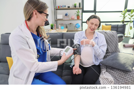 Excitement fills the air as a doctor checks the blood pressure of a pregnant woman in a cozy living room 136194981