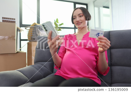 Excitement fills the air as a pregnant woman shops online in her cozy home surrounded by moving boxes Excitement fills the air as a pregnant woman shops online in her cozy home surrounded by moving boxes 136195009