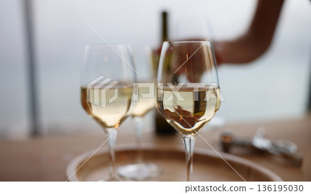 Elegant wine glasses filled with crisp white wine on a serene table by the water during a calm afternoon gathering Elegant wine glasses filled with crisp white wine on a serene table by the water during a calm afternoon gathering 136195030