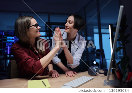 Two colleagues celebrate success in a modern office during an evening brainstorming session filled with excitement and teamwork Two colleagues celebrate success in a modern office during an evening brainstorming session filled with excitement and teamwork 136195084