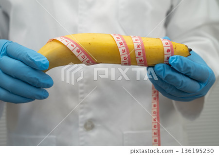 Doctor holding a banana with measuring tape, penis health. 136195230