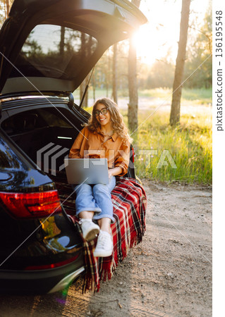 Happy woman working with laptop from the car trunk or boot in camper sunny summer park. 136195548