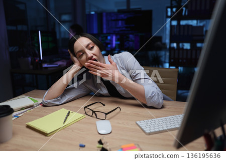 Late night work creates a sleepy atmosphere for a focused professional in a modern office space 136195636