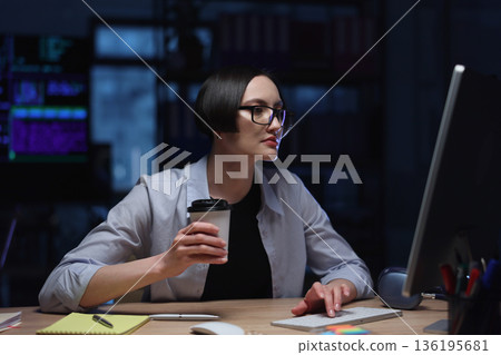 Focused woman working late at night with a coffee cup at her desk in a cozy tech environment Focused woman working late at night with a coffee cup at her desk in a cozy tech environment 136195681