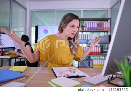 Frustrated professional expresses concerns during a busy workday at a modern office setting filled with colorful files 136195725