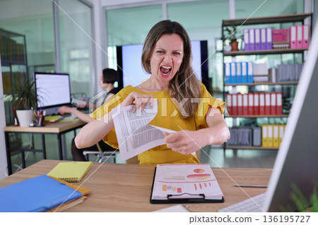Frustration unveiled in the modern office as a woman tears reports during a stressful workday 136195727