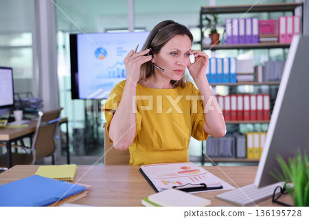 Woman in a yellow dress analyzing data at a modern office space in the afternoon while on a call 136195728