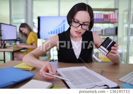 Busy professional reviews important documents while colleague works on a project in a modern office space during daytime Busy professional reviews important documents while colleague works on a project in a modern office space during daytime 136195733