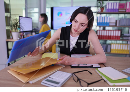 Focused woman organizes documents and analyzes data in a modern office setting during the day 136195746