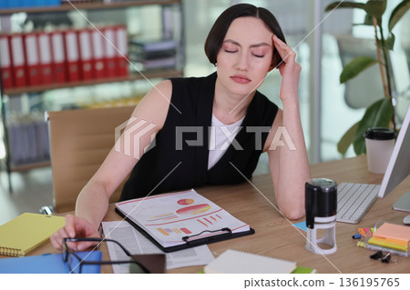 Stressed professional reviews data in a modern office filled with paperwork and bright colors Stressed professional reviews data in a modern office filled with paperwork and bright colors 136195765