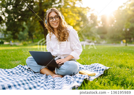 Portrait of woman sitting on green grass in park with legs crossed. Concept for education, business. Portrait of woman sitting on green grass in park with legs crossed. Concept for education, business. 136195989